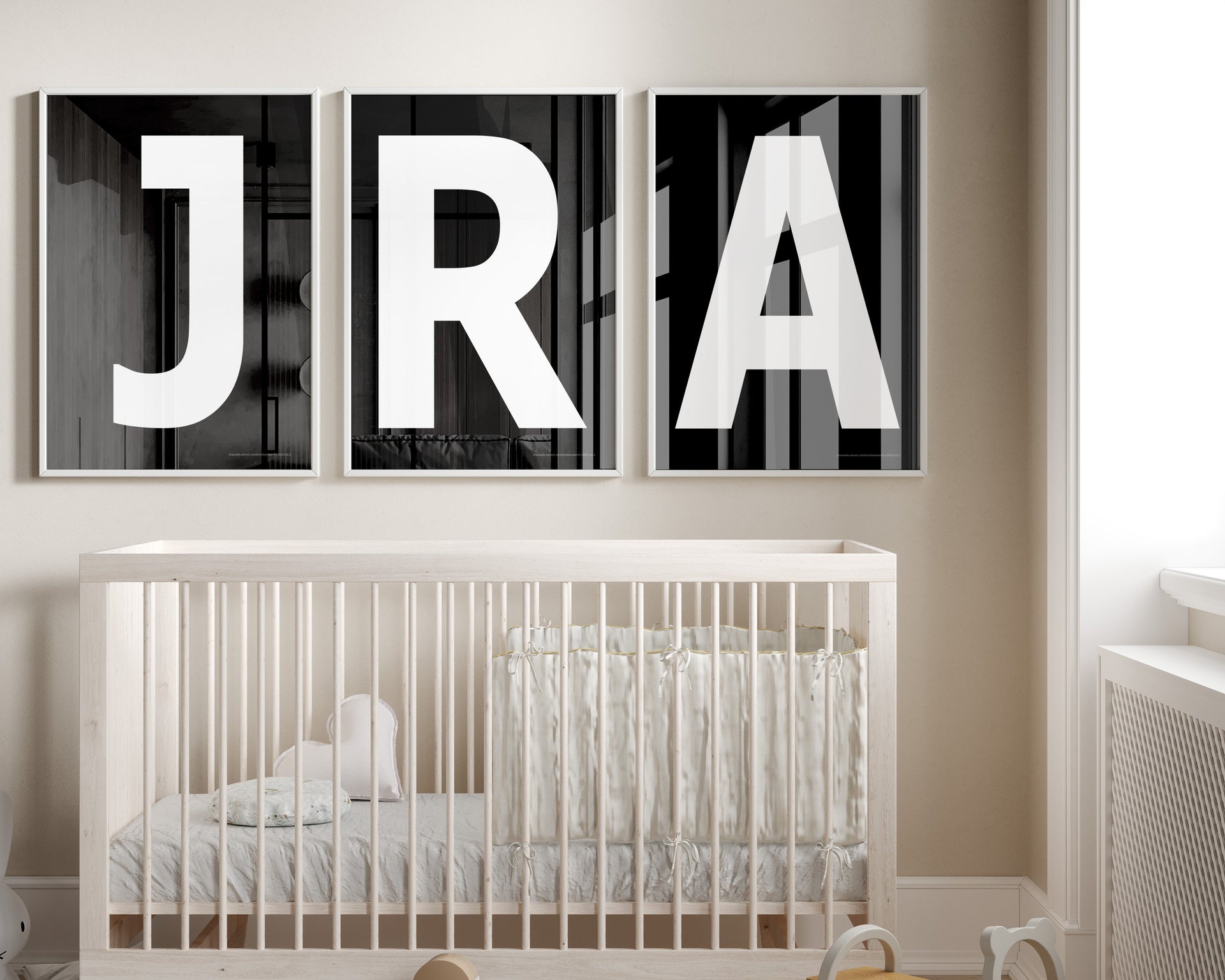 Three framed white and black letter art prints spelling out a baby's initials or monogram hanging above a crib in a neutral nursery.