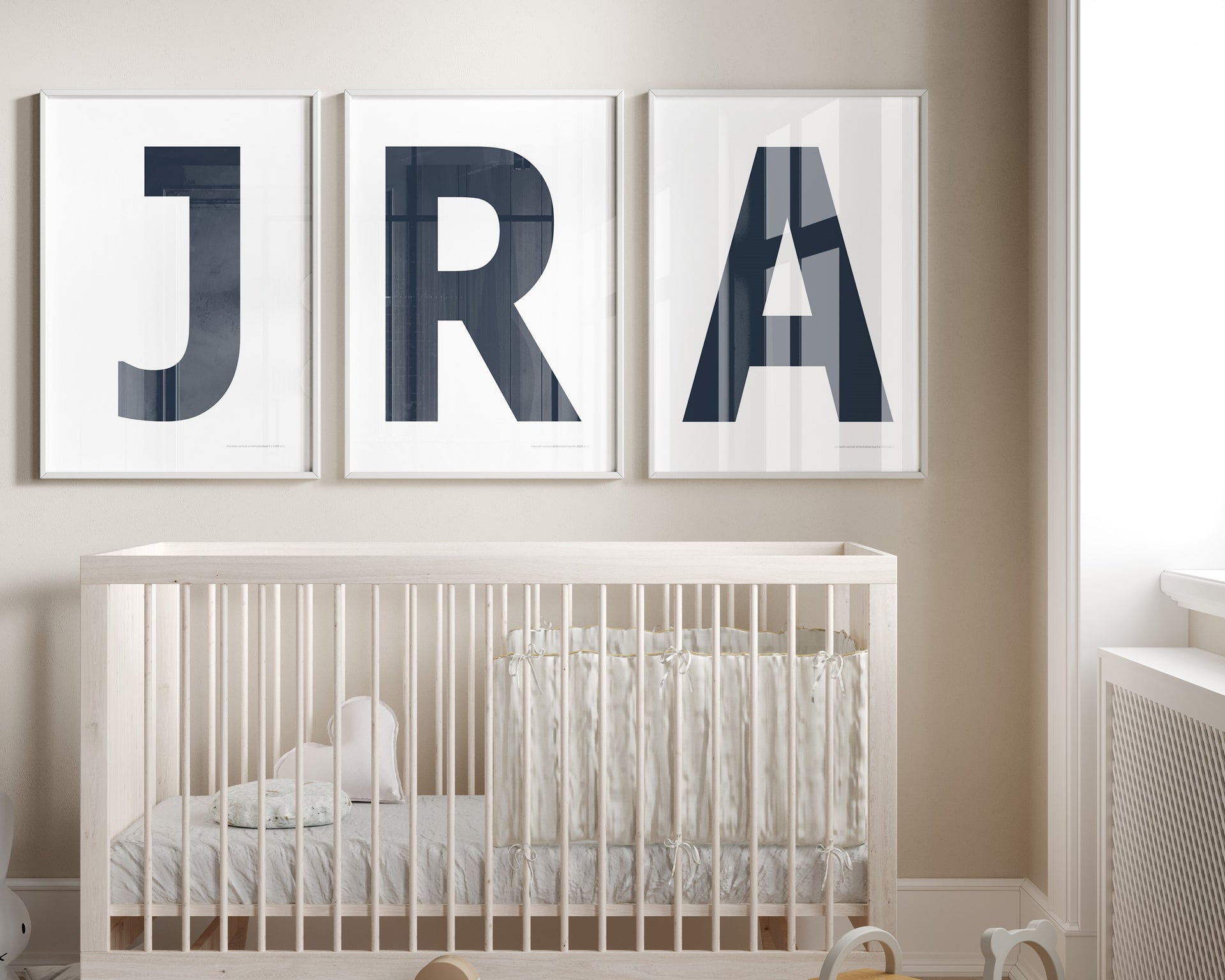 Three framed white and navy blue letter art prints spelling out a baby's initials or monogram hanging above a crib in a neutral nursery.