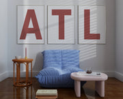 Three large framed Nantucked red and white letter art prints spelling out ATL hanging above a blue chair.