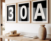 Three framed black and white number and letter art prints spelling out 30A hanging above a table in a boho beach entryway.