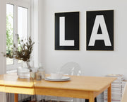 Two framed black and white letter art prints spelling out LA hanging in a bright white dining room.