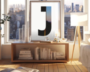 Framed white and black letter art print in living room with a city view.