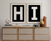 Two framed black and white letter art prints spelling out HI hanging above a credenza in a hallway or entryway.