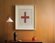 Framed white and Nantucket red plus sign art print featuring an iniital hanging above a table in a mid century entrway or hallway.