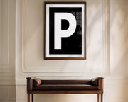 Oversized framed black and white letter art print haning above a bence in a formal entryway or hallway.