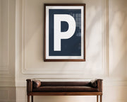 Oversized framed navy blue and white letter art print haning above a bence in a formal entryway or hallway.