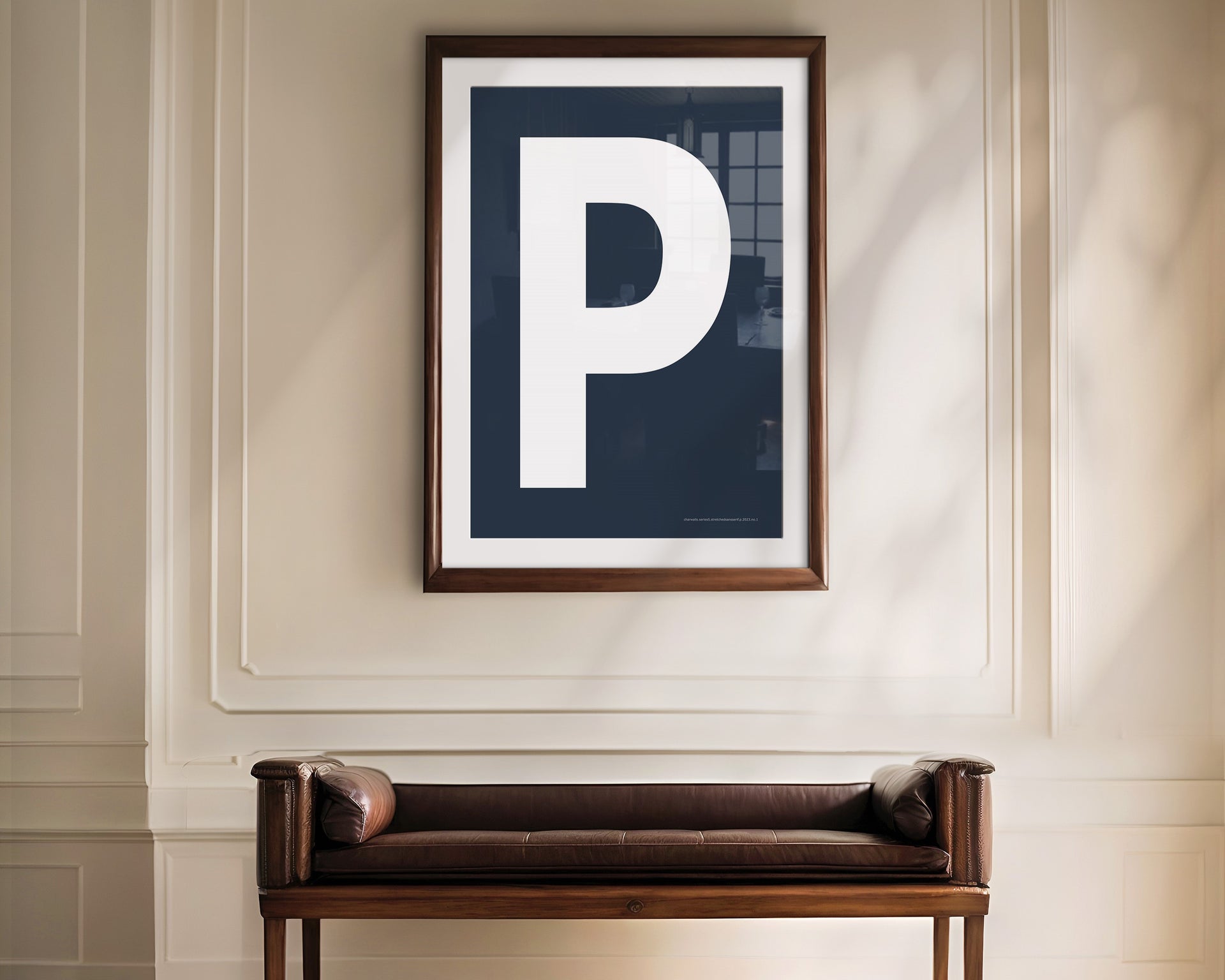 Oversized framed navy blue and white letter art print haning above a bence in a formal entryway or hallway.