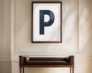 Oversized framed navy blue and white letter art print haning above a bence in a formal entryway or hallway.