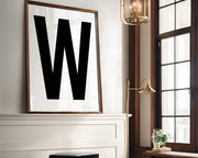 Oversized framed white and black letter art print above a mantle in a living room.