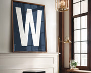Oversized framed white and navy blue letter art print above a mantle in a living room.