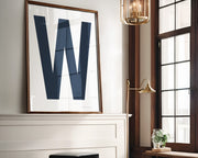 Oversized framed white and navy blue letter art print above a mantle in a living room.