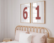 Two framed Nantucket red and white number frames featuring a girl's jersey numbers hanging above the bed.