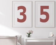Two framed Nantucket red and white number art prints showing a jersey number hanging above bed and desk.