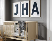 3 Framed letter art prints featuring navy blue and white initials hanging above a crib in a gray boy nursery.