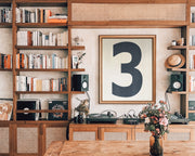 Modern library featuring a framed number art print above a mid century credenza surrounded by book shelves.