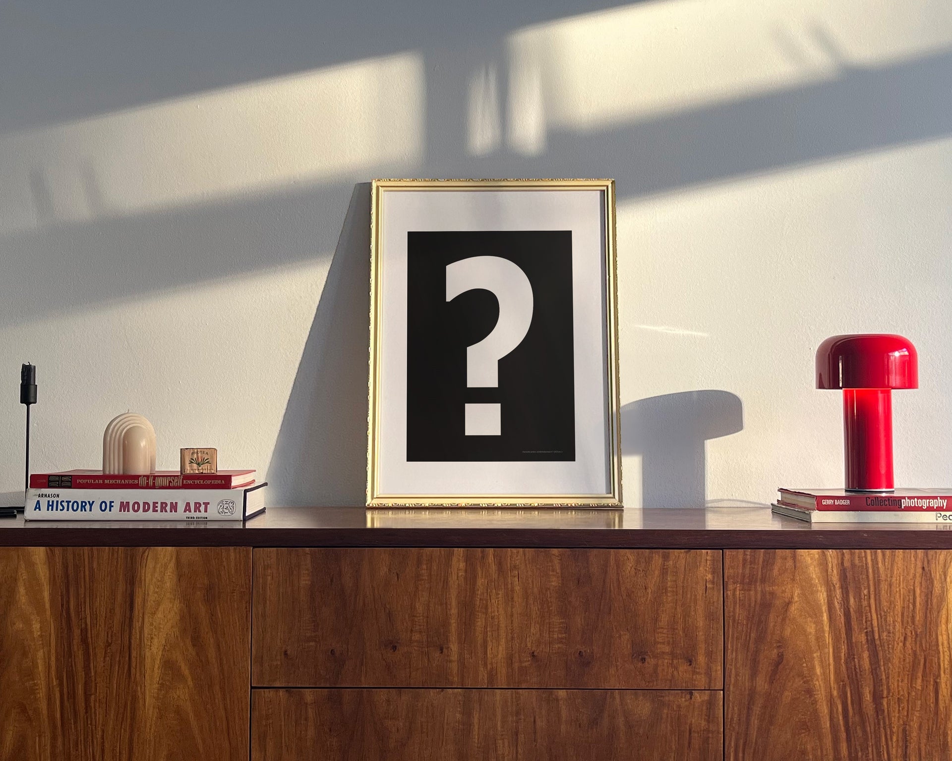 Small framed black and white question mark art print on a midcentury credenza.