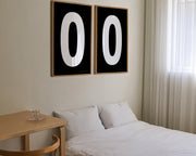 Two framed black and white number zero art prints hanging above a bed in a modern bedroom.
