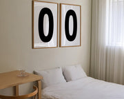 Two framed black and white number zero art prints hanging above a bed in a modern bedroom.