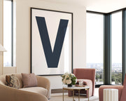 Oversized framed navy blue and white letter V art print hanging in a modern living room.