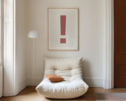 Large framed Nantucket red and white exclamation point art print hanging above a modern chair in a living room.