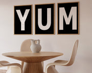 Three framed black and white letter art prints spelling out the word YUM hanging in a modern dining room.