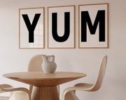 Three framed black and white letter art prints spelling out the word YUM hanging in a modern dining room.