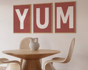 Three framed Nantucket red and white letter art prints spelling out the word YUM hanging in a modern dining room.