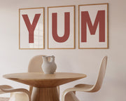 Three framed Nantucket red and white letter art prints spelling out the word YUM hanging in a modern dining room.
