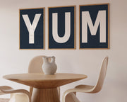 Three framed navy blue and white letter art prints spelling out the word YUM hanging in a modern dining room.