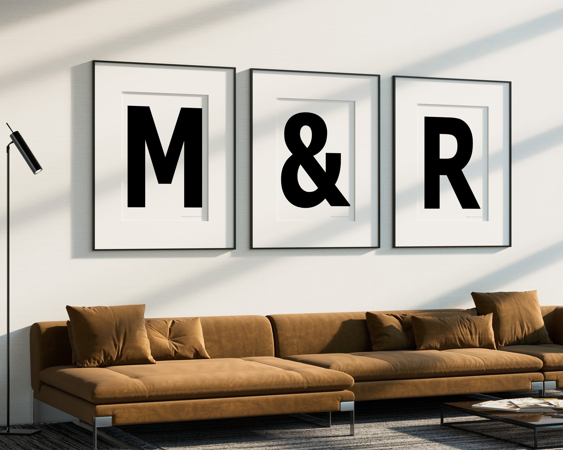 Three oversized framed black and white letter and ampersand art prints spelling out M&R hanging above a modern sofa.