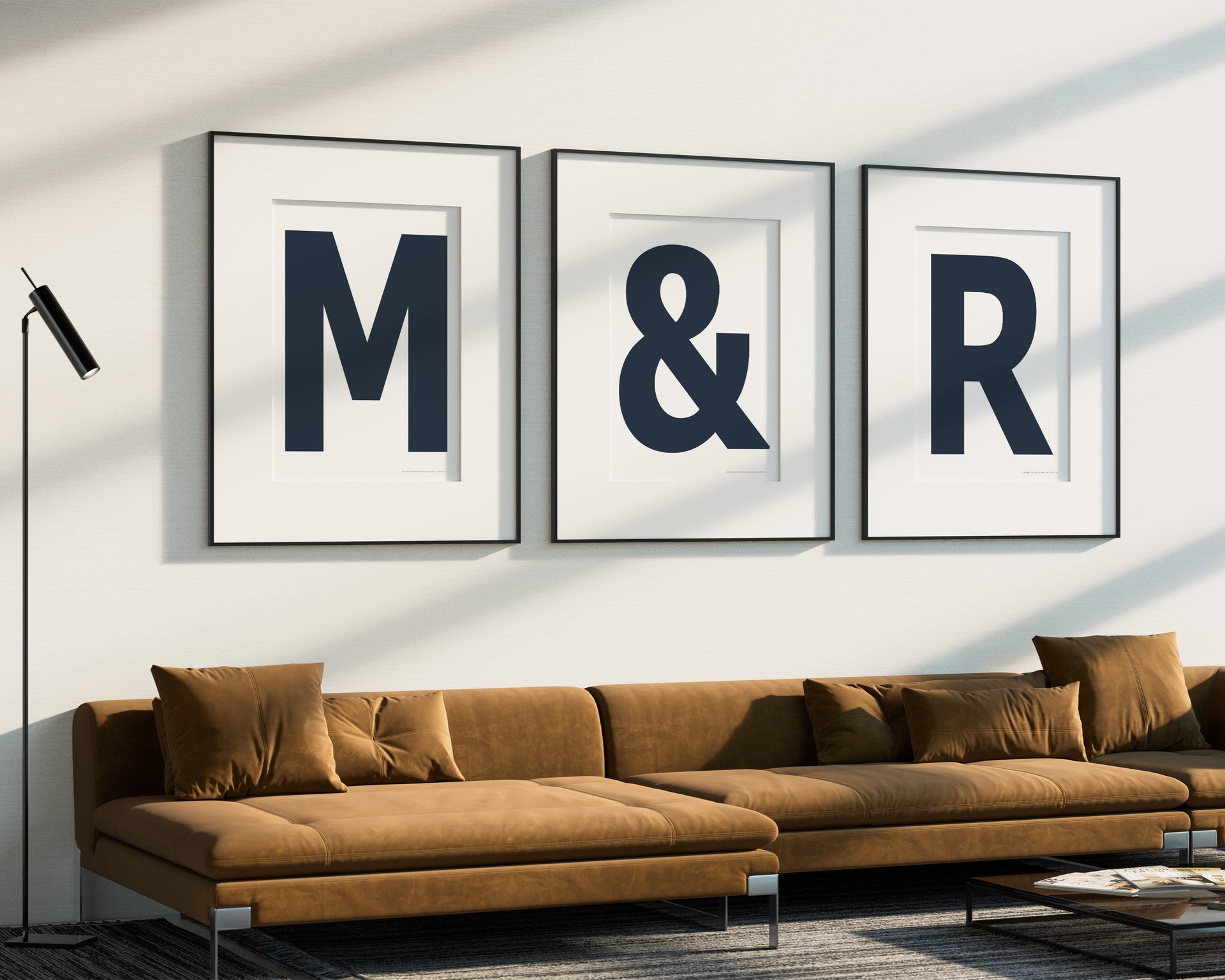 Three oversized navy blue and white letter and ampersand art prints spelling out M&R hanging above a modern sofa.