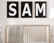 Three framed black and white letter art prints spelling out the name SAM hanging above a crib in a neutral nursery.