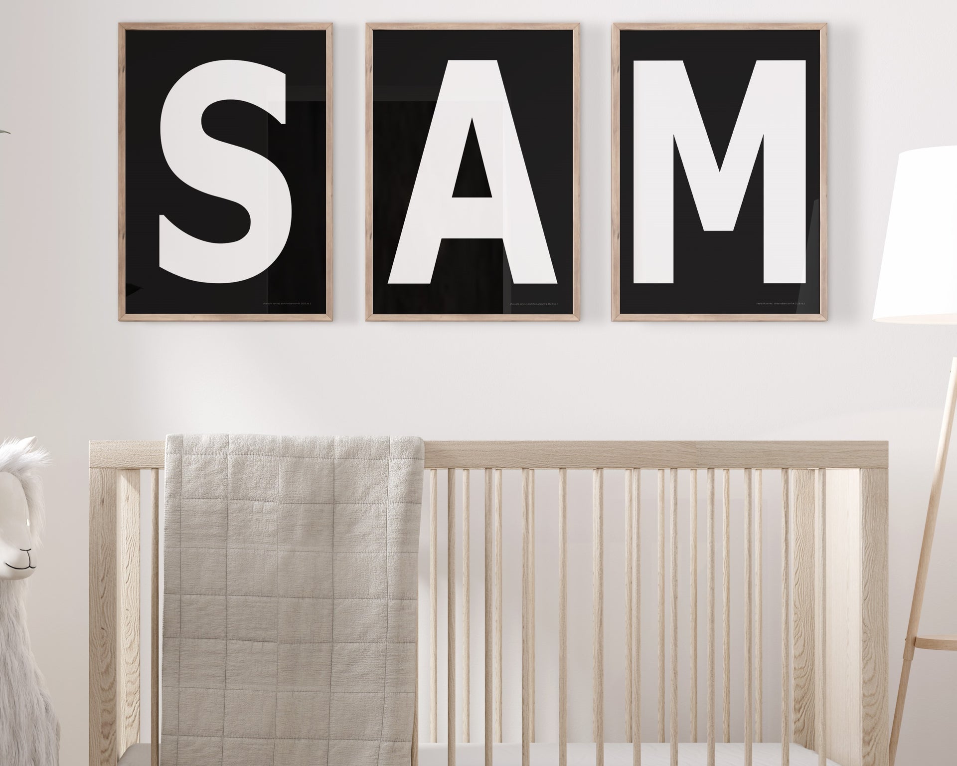 Three framed black and white letter art prints spelling out the name SAM hanging above a crib in a neutral nursery.