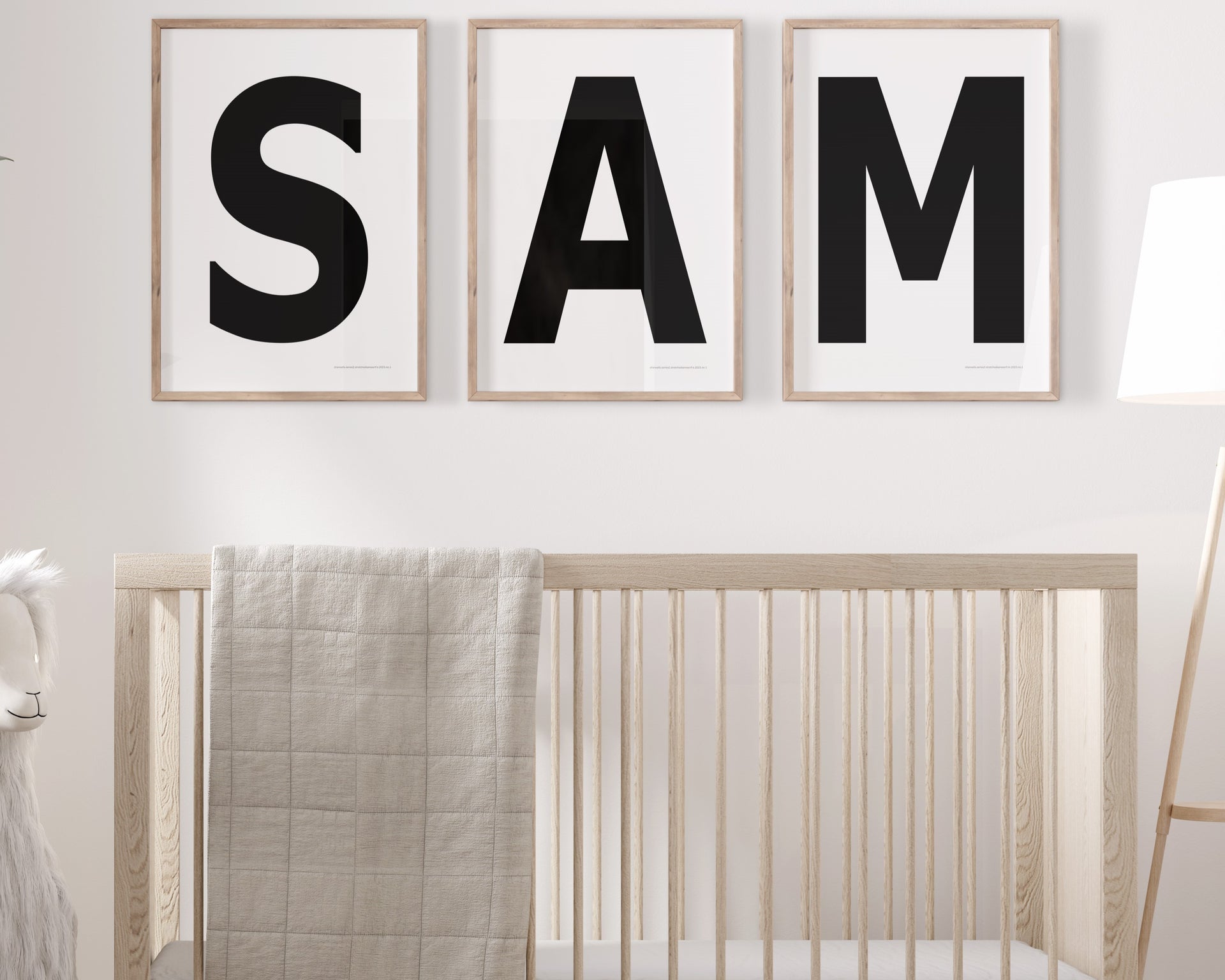 Three framed black and white letter art prints spelling out the name SAM hanging above a crib in a neutral nursery.