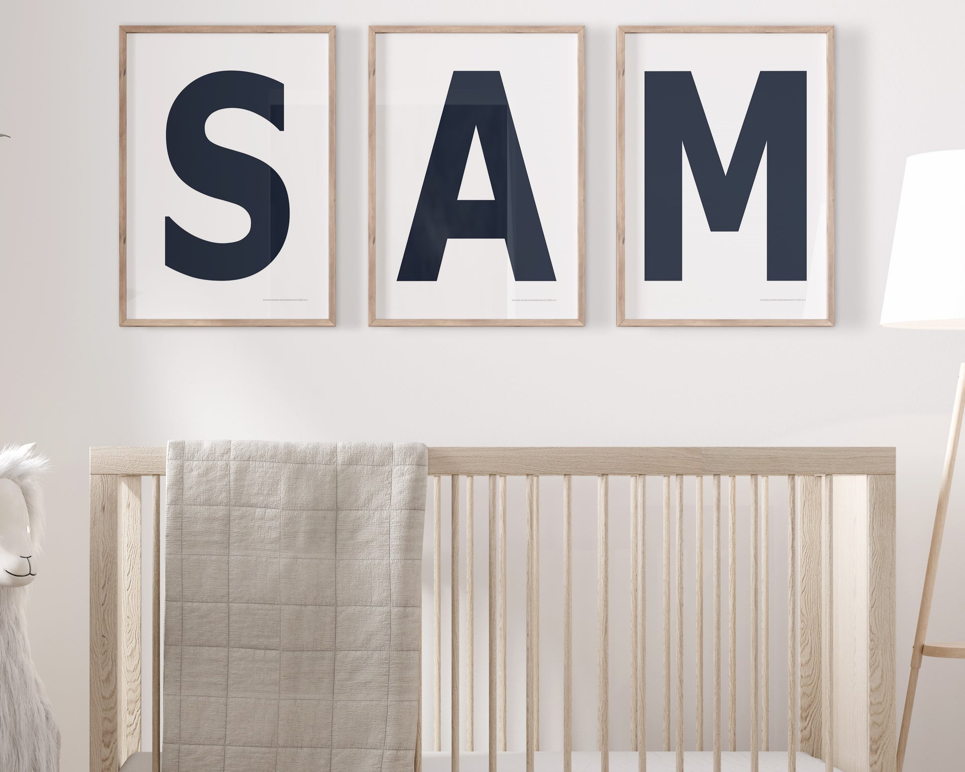 Three framed navy blue and white letter art prints spelling out the name SAM hanging above a crib in a neutral nursery.