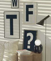 Four framed navy blue and white letter and question mark art prints spelling out WTF? hanging on the wall in a modern living room.