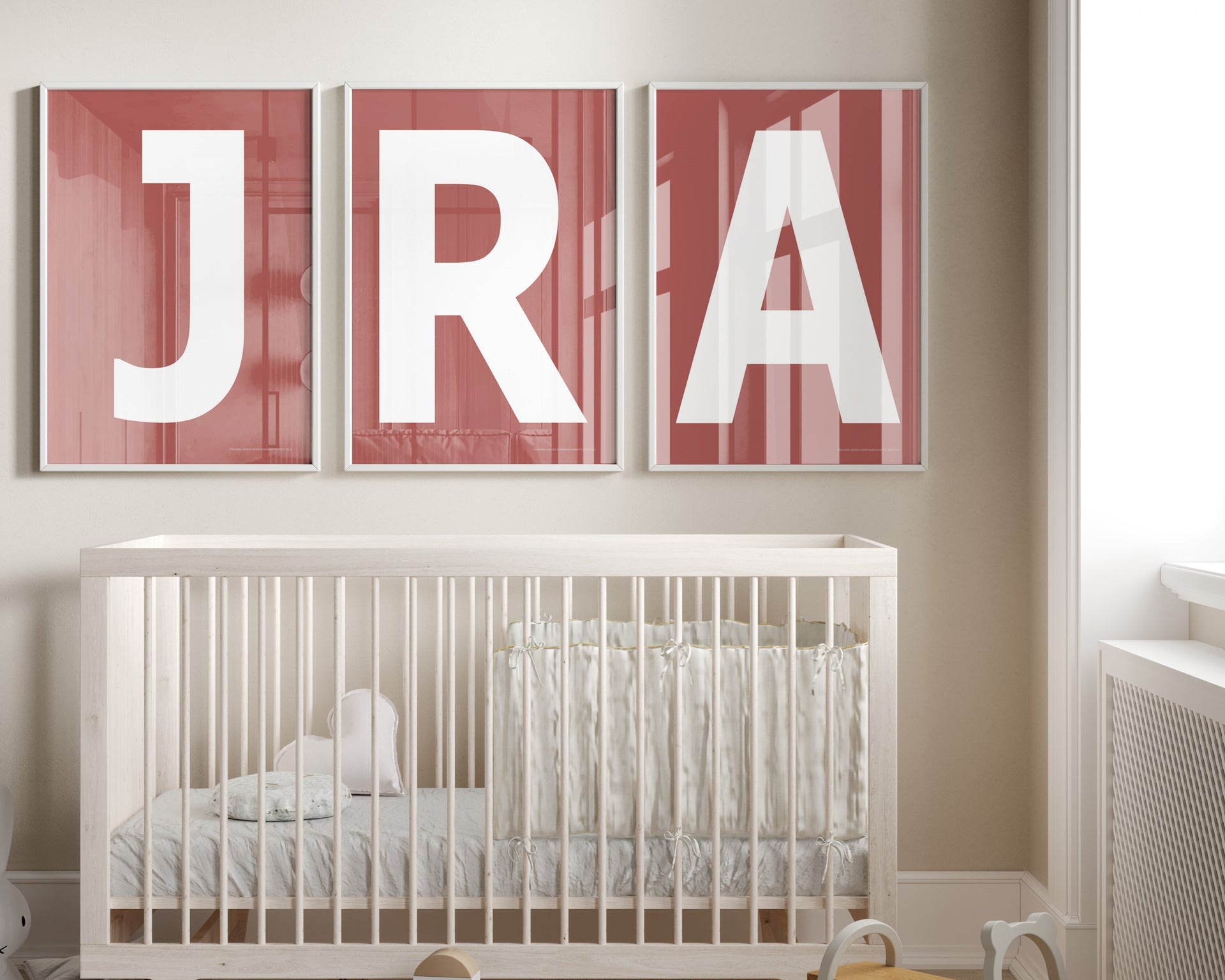 Three framed white and Nantucket red letter art prints spelling out a baby's initials or monogram hanging above a crib in a neutral nursery.