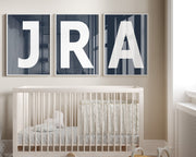 Three framed navy blue letter art prints spelling out a baby's initials or monogram hanging above a crib in a neutral nursery.