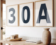 Three framed navy blue and white number and letter art prints spelling out 30A hanging above a table in a boho beach entryway.