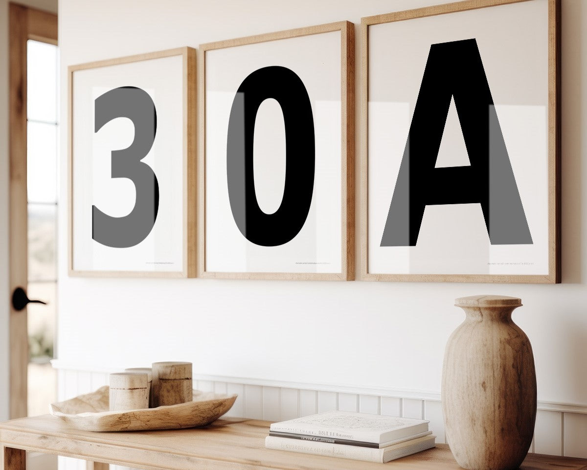 Three framed black and white number and letter art prints spelling out 30A hanging above a table in a boho beach entryway.