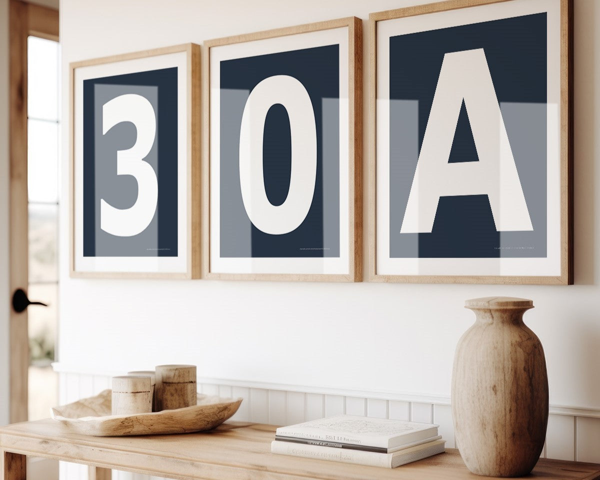 Three framed navy blue and white number and letter art prints spelling out 30A hanging above a table in a boho beach entryway.