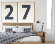 Two large framed navy blue and white number art frames showcasing a boy's jersey number hanging above his bed with a plaid blanket.