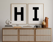 Two framed black and white letter art prints spelling out HI hanging above a credenza in a hallway or entryway.