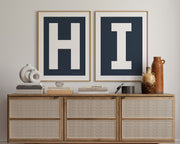 Two framed navy blue and white letter art prints spelling out HI hanging above a credenza in a hallway or entryway.