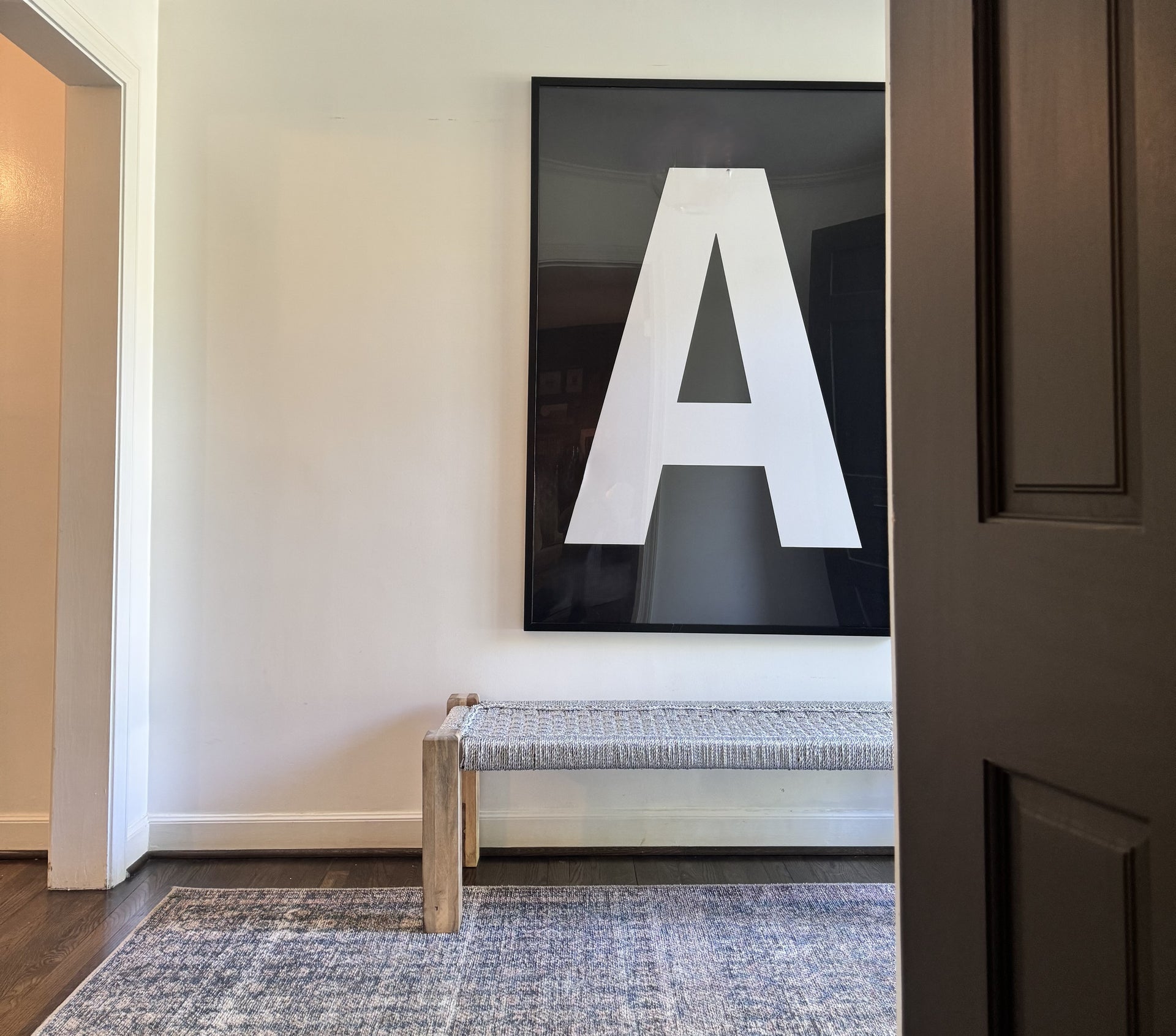 Oversized letter art print featuring a white A on a black background hung above a silver bench in a home entryway.