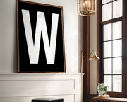 Oversized framed white and black letter art print above a mantle in a living room.