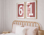 Two framed Nantucket red and white number frames featuring a girl's jersey numbers hanging above the bed.