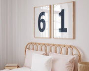 Two framed Nantucket red and white number frames featuring a girl's jersey numbers hanging above the bed.