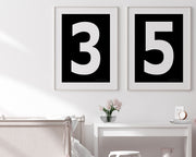 Two framed black and white number art prints showing a jersey number hanging above bed and desk.