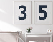 Two framed navy blue and white number art prints showing a jersey number hanging above bed and desk.